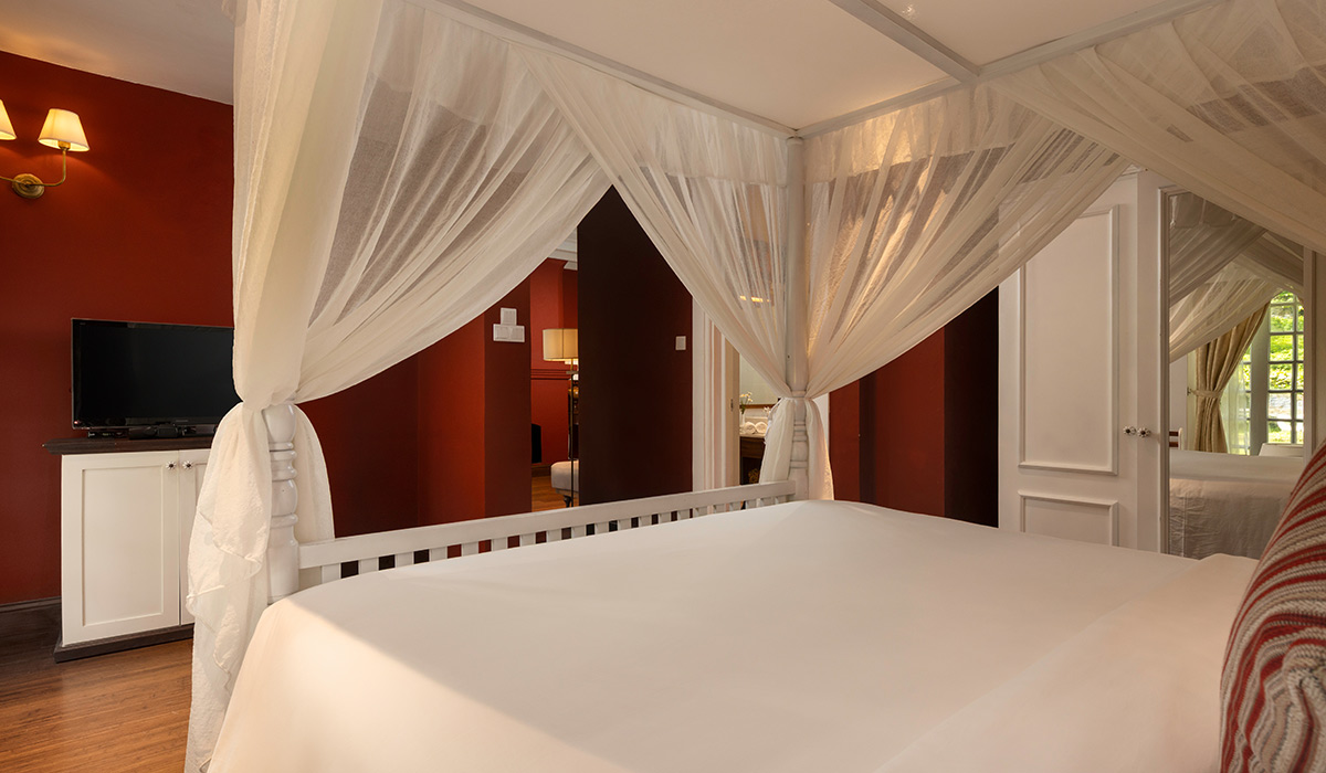 A Heritage Suite with a four-poster bed hung with white nets and deep red walls