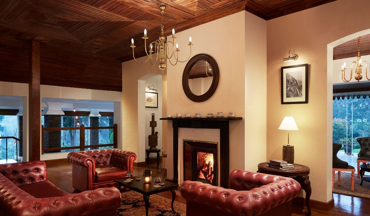 A lounge with red leather chesterfields around a lit fireplace under a timber ceiling